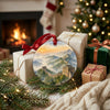 Round landmark ornament styled near wrapped holiday gifts in front of a warm glowing fireplace.