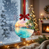 Scenic tropical holiday ornament hanging in front of a bright snowy winter window.