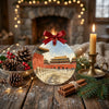 Festive holiday ornament styled on a rustic tabletop beside decorative pinecones and warm candlelight.