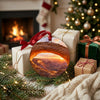 Holiday travel ornament resting alongside wrapped gifts near a warm glowing fireplace