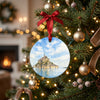 Holiday ceramic keepsake hanging on a lit Christmas tree branch with festive lights.