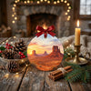 Desert landscape ornament styled on a rustic holiday table alongside a natural pinecone and a glowing candle.