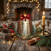 Festive holiday decoration resting on a tabletop beside natural pinecone accents and a glowing candle.